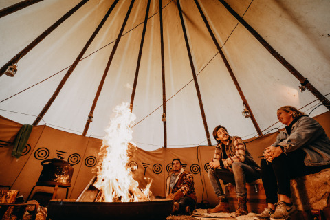 Drie personen zitten rond een kampvuur in een gezellige glamping yurt met traditionele patronen in Drenthe.