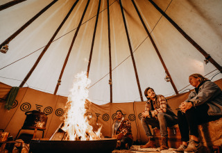 Drie personen zitten rond een kampvuur in een gezellige glamping yurt met traditionele patronen in Drenthe.