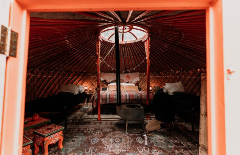 Binnenkant van een gezellige Winterwoods-yurt in Drenthe met bedden, houtkachel en folkloristische tafels.