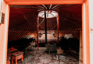 Binnenkant van een gezellige Winterwoods-yurt in Drenthe met bedden, houtkachel en folkloristische tafels.