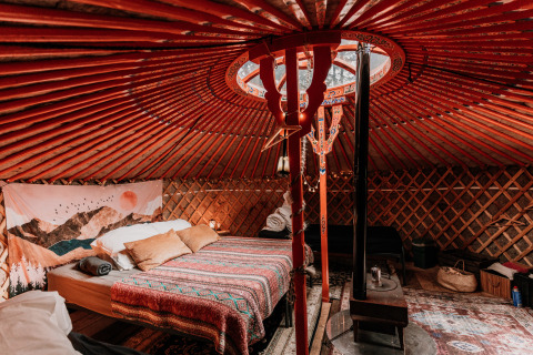 Gezellige binnenkant van een yurt bij glamping Winterwoods in Drenthe, met tweepersoonsbed en houtkachel.