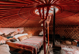 Gezellige binnenkant van een yurt bij glamping Winterwoods in Drenthe, met tweepersoonsbed en houtkachel.