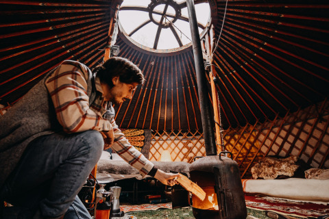 Man maakt vuur in houtkachel binnen een gezellige yurt, luxe winterglamping accommodatie in Drenthe.