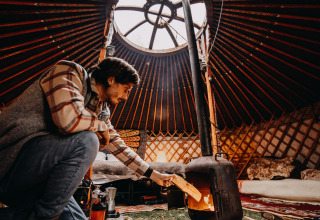 Man maakt vuur in houtkachel binnen een gezellige yurt, luxe winterglamping accommodatie in Drenthe.