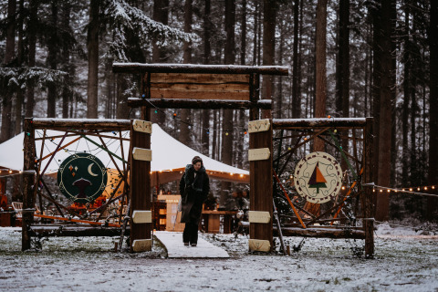 Ingang van Winterwoods glamping in besneeuwd bos, houten poort en sfeerverlichting zichtbaar.