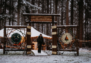 Ingang van Winterwoods glamping in besneeuwd bos, houten poort en sfeerverlichting zichtbaar.