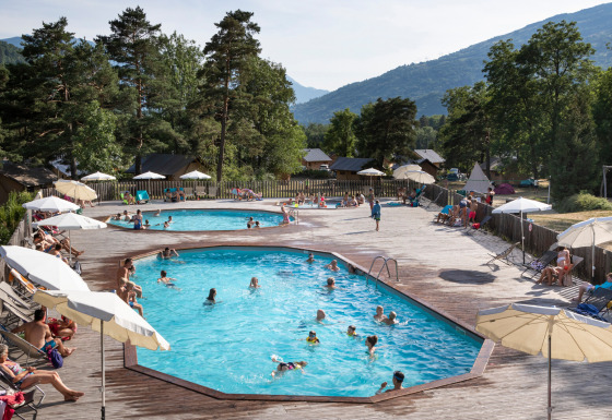 Piscines extérieures avec vacanciers au Huttopia Bourg-Saint-Maurice - Glamping Savoie, entouré de montagnes.