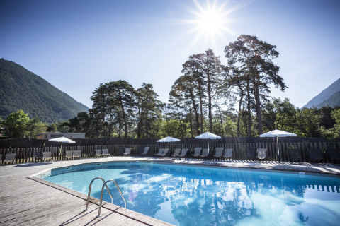 Piscina all'aperto al Huttopia Bourg-Saint-Maurice Glamping con lettini, ombrelloni e vista sulle montagne.