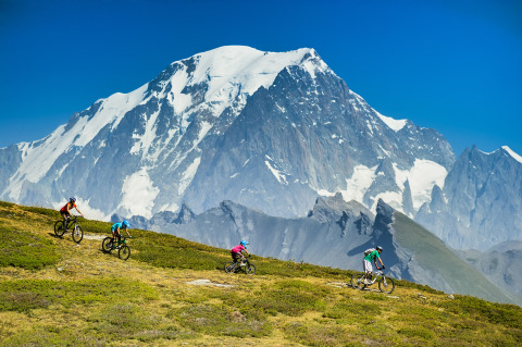 Cykelentusiaster kører mountainbike med udsigt til sneklædte Alperne nær Huttopia Bourg-Saint-Maurice.