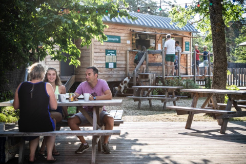 Familia disfruta de una comida en una mesa de pícnic frente a una cabaña de madera en Huttopia Bourg-Saint-Maurice.