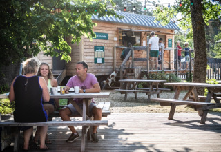 Familia disfruta de una comida en una mesa de pícnic frente a una cabaña de madera en Huttopia Bourg-Saint-Maurice.