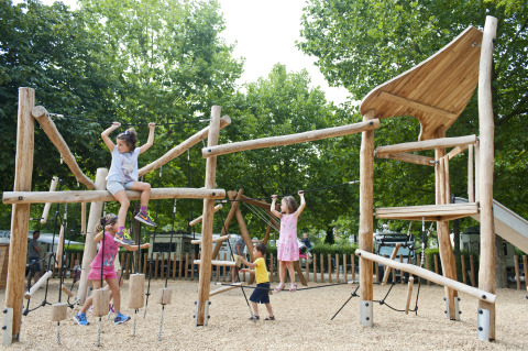 Bambini giocano su un parco giochi in legno circondato da alberi a Huttopia Bourg-Saint-Maurice Glamping Savoie.