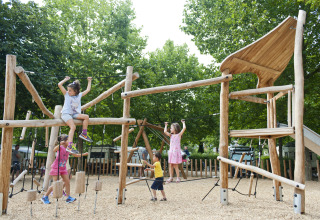 Niños juegan en un parque infantil de madera rodeado de árboles en Huttopia Bourg-Saint-Maurice Glamping Savoie.