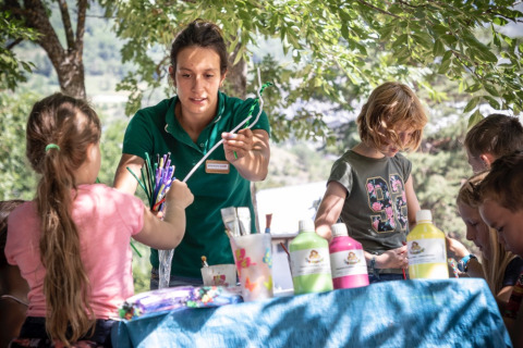 Niños realizando manualidades al aire libre junto a una adulta en Huttopia Bourg-Saint-Maurice Glamping Savoie.