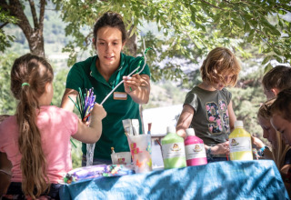 Niños realizando manualidades al aire libre junto a una adulta en Huttopia Bourg-Saint-Maurice Glamping Savoie.