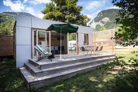 Glamping indkvartering med træterrasse, stole og parasol ved Huttopia Bourg-Saint-Maurice, omgivet af bjerge.