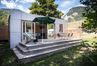 Glamping indkvartering med træterrasse, stole og parasol ved Huttopia Bourg-Saint-Maurice, omgivet af bjerge.