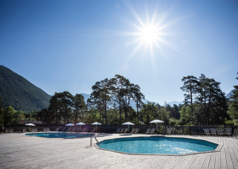 Piscina esterna a Huttopia Bourg-Saint-Maurice - Glamping Savoie, circondata da montagne e alberi al sole.