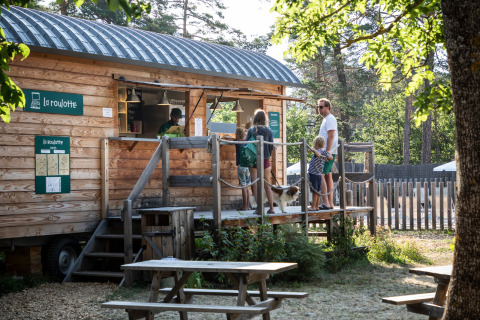 Gezin met hond bij houten eetkraam op Huttopia Bourg-Saint-Maurice - Glamping Savoie, midden in de natuur.