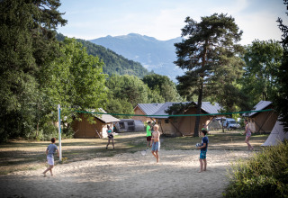 Children play volleyball on a sandy court, with glamping tents and mountains visible at Huttopia Bourg-Saint-Maurice.