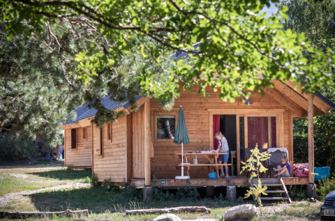 Famiglia si gode il tempo libero sulla veranda di una baita in legno a Huttopia Bourg-Saint-Maurice Glamping Savoie.