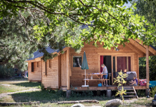 Gezin geniet op de veranda van een houten huisje bij Huttopia Bourg-Saint-Maurice - Glamping Savoie.