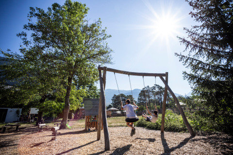 Zwei Kinder schaukeln unter der Sonne auf dem Spielplatz bei Huttopia Bourg-Saint-Maurice - Glamping Savoie.