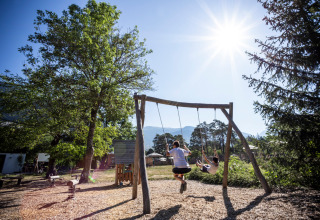 Deux enfants se balancent au soleil sur l'aire de jeux de Huttopia Bourg-Saint-Maurice - Glamping Savoie.