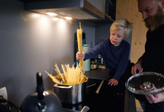 Kind en volwassene koken samen pasta in een tiny house bij Wellnester Camping bij Losheim am See, Saarland.