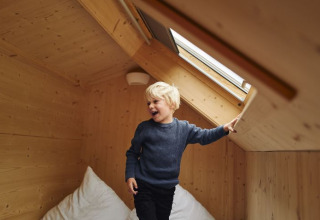 Un bambino gioca in una tiny house rivestita in legno con lucernario al Wellnester Camping Saarland.