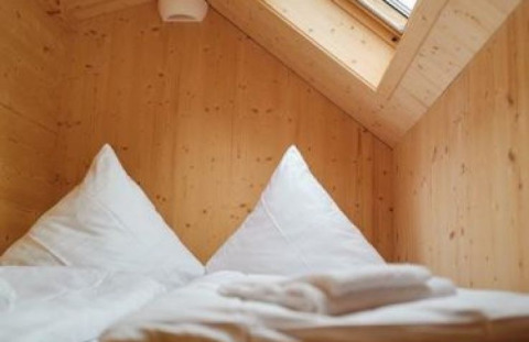 Vista interna di una tiny house glamping al Wellnester Camping vicino a Losheim am See, con pareti in legno e lucernario.