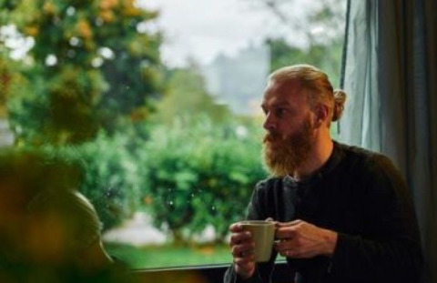 Mand med skæg drikker kaffe og nyder udsigten fra Wellnester Camping ved Losheim am See, Tiny houses Saarland.