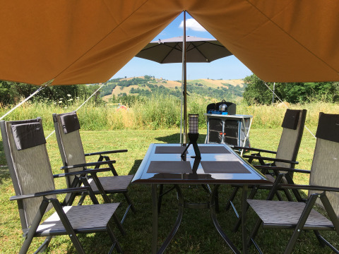 Zona de glamping exterior en Agriturismo Camping Le Marche con mesa, sillas y vista a las colinas.
