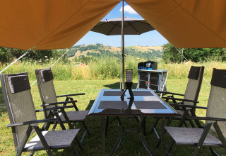 Zona de glamping exterior en Agriturismo Camping Le Marche con mesa, sillas y vista a las colinas.