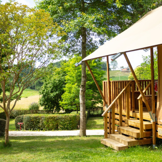 Hébergement glamping au Camping Pré Fixe dans les Pyrénées, tente lodge avec terrasse en bois, verdure.