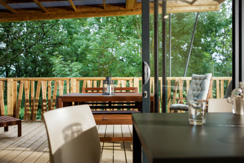 Modern glamping lodge with wooden terrace, dining table, and forest view at Camping Pré Fixe, Pyrenees.