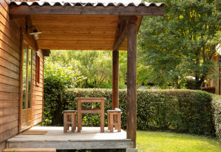 Chalet in legno con veranda e panche al Camping Pré Fixe - Lodges nei Pirenei, circondato dal verde.