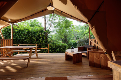 Houten veranda met picknicktafel en zithoek in een glamping lodge bij Camping Pré Fixe in de Pyreneeën.