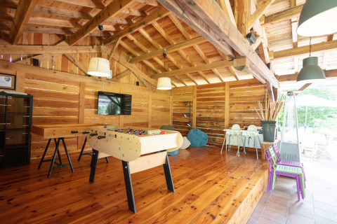 Sala de juegos interior con futbolín, TV y sillas para niños en Camping Pré Fixe - Lodges en los Pirineos.