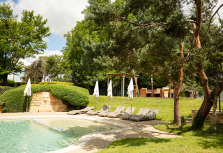 Outdoor pool with sun loungers and umbrellas surrounded by lush greenery at Camping Pré Fixe in the Pyrenees.