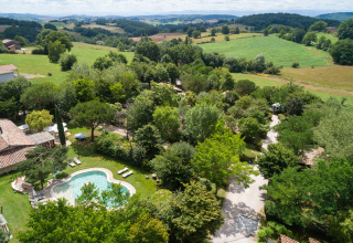 Vista aérea de Camping Pré Fixe con lodges y piscina en los Pirineos, rodeado de naturaleza verde y campos.