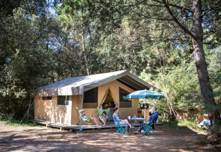 Famille en glamping à Huttopia Oléron les Pins, Nouvelle-Aquitaine, relaxant devant une tente aménagée.