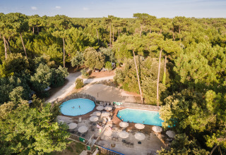 Aerial view of Huttopia Oléron les Pins glamping site, featuring pools, sun umbrellas, and dense forest surroundings.