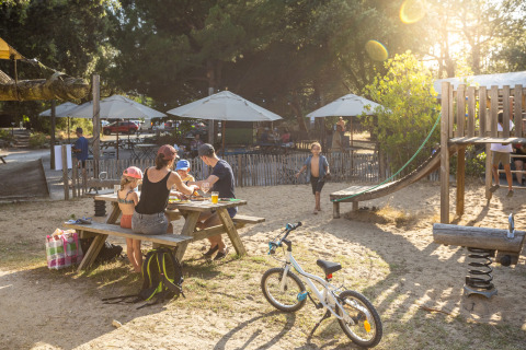Familia haciendo picnic junto a zona de juegos en Huttopia Oléron les Pins Glamping Nouvelle-Aquitaine.