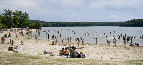 Spiaggia di Huttopia Lac de Sillé - Glamping Pays de la Loire, con molte persone in acqua e sulla sabbia.
