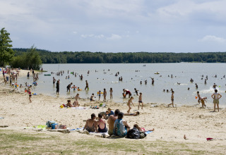 Beach at Huttopia Lac de Sillé - Glamping Pays de la Loire, with many people swimming and relaxing on sand.