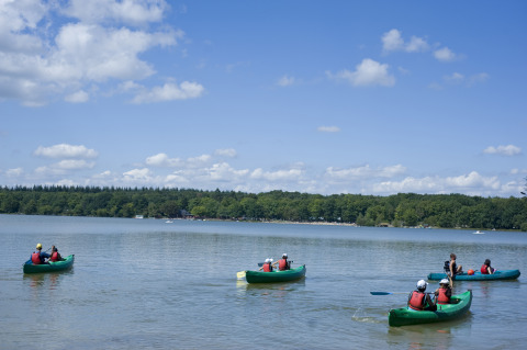 Gasten kanoën op het meer bij Huttopia Lac de Sillé - Glamping Pays de la Loire onder een stralende lucht.