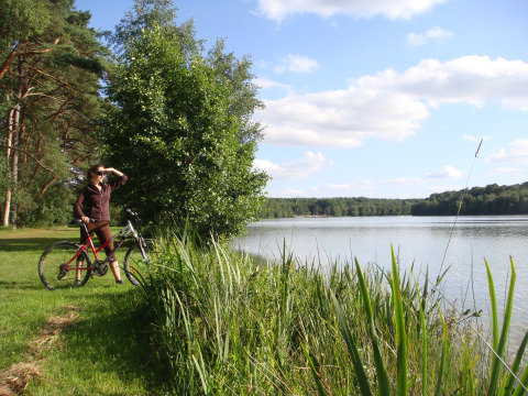 Vrouw met fiets kijkt uit over het meer bij Huttopia Lac de Sillé - Glamping Pays de la Loire, Frankrijk.