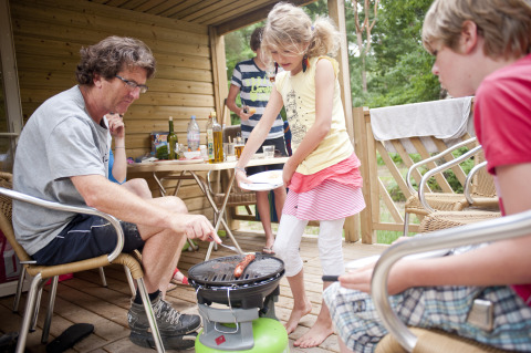 Familie nyder udendørs grill på træterrasse ved Huttopia Lac de Sillé - Glamping Pays de la Loire.