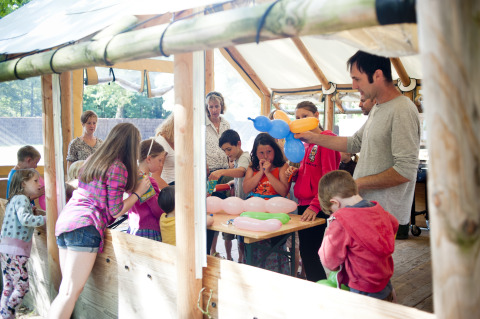 Enfants et adultes fabriquent des animaux en ballon sous un abri en bois à Huttopia Lac de Sillé glamping.